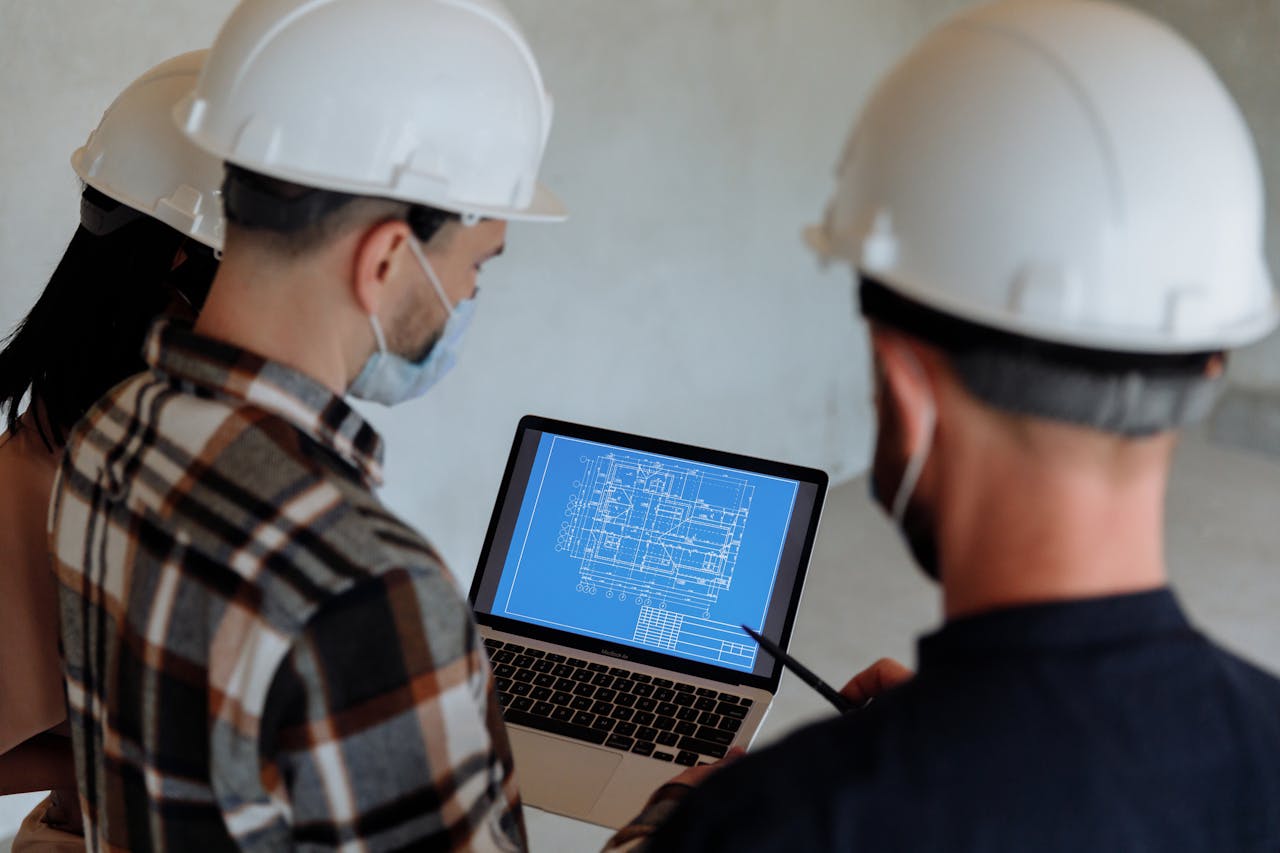 Project managers wearing hard hats, reviewing a blueprint on a laptop