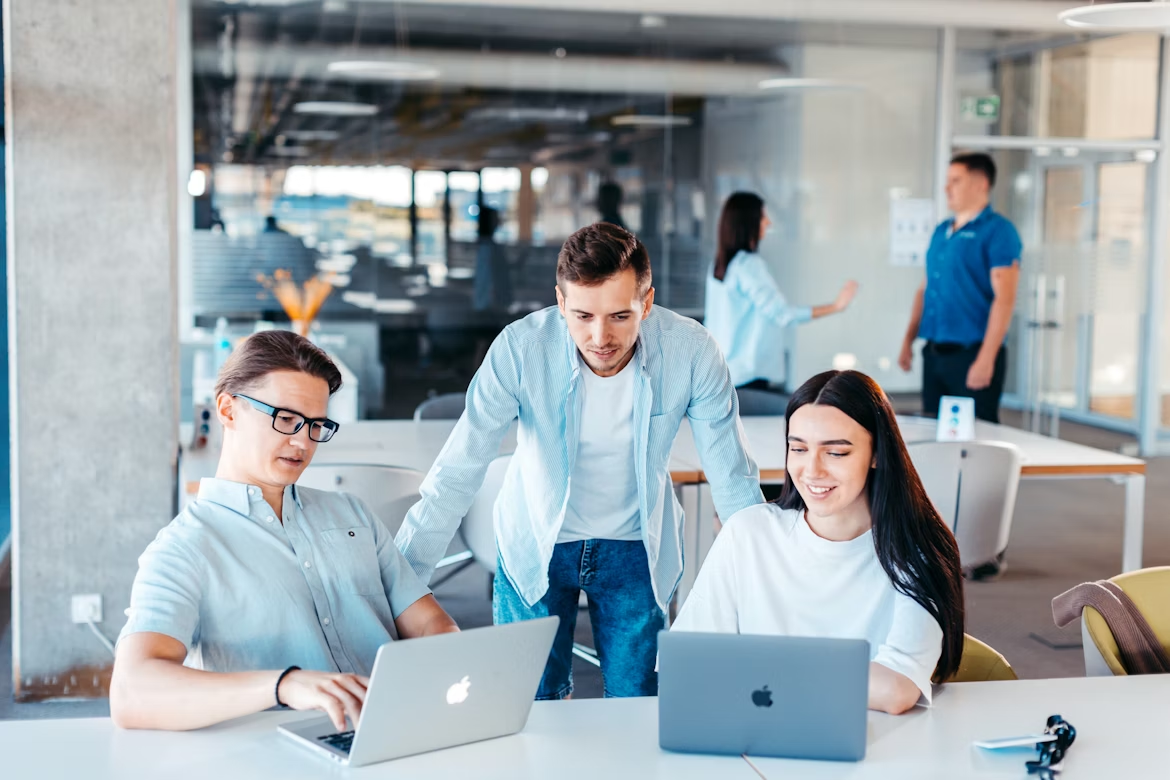 Two men and a woman working on MacBooks in an open office